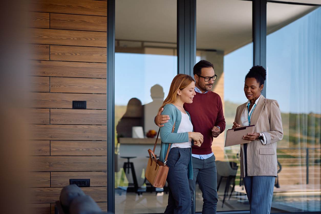 Smiling couple and their real estate agent analyzing paperwork during open house day. Smiling couple and their real estate agent analyzing paperwork during open house day.